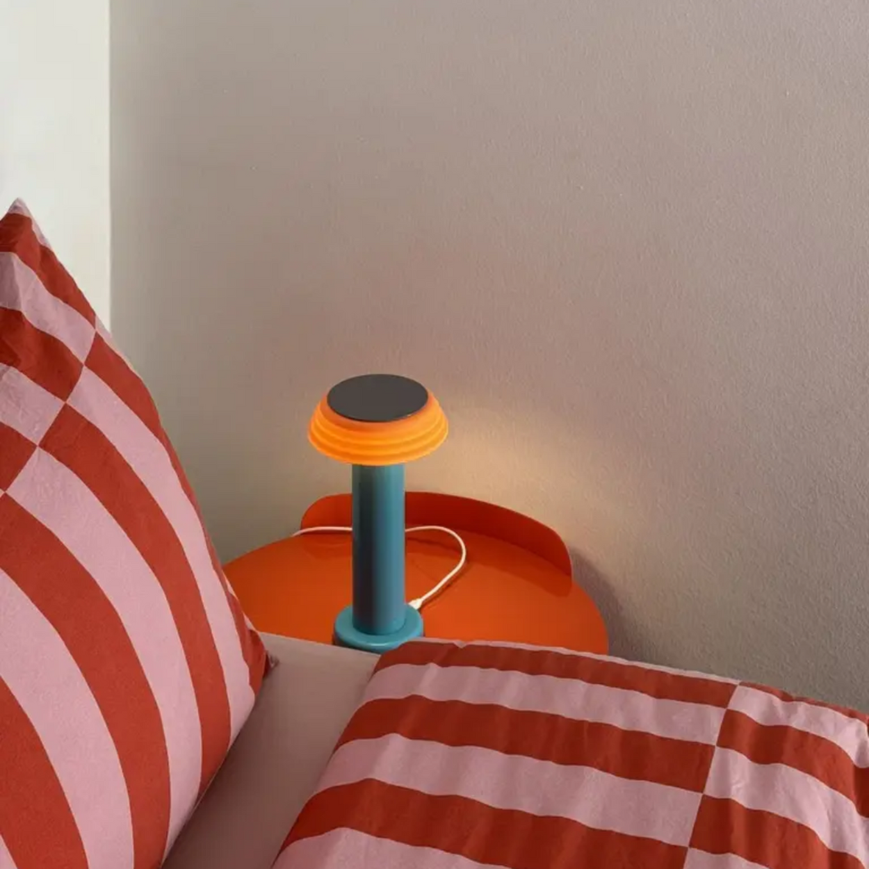 Small orange and blue lamp on a bedside table with striped bedding.