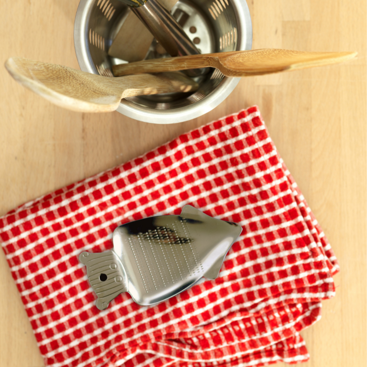 Metallic grater on a red and white checkered towel with a wooden spoon in the background.