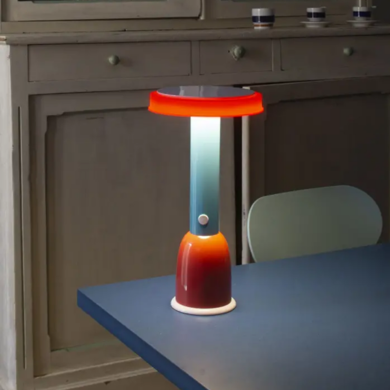 Colorful table lamp on a blue table with a wooden cabinet in the background