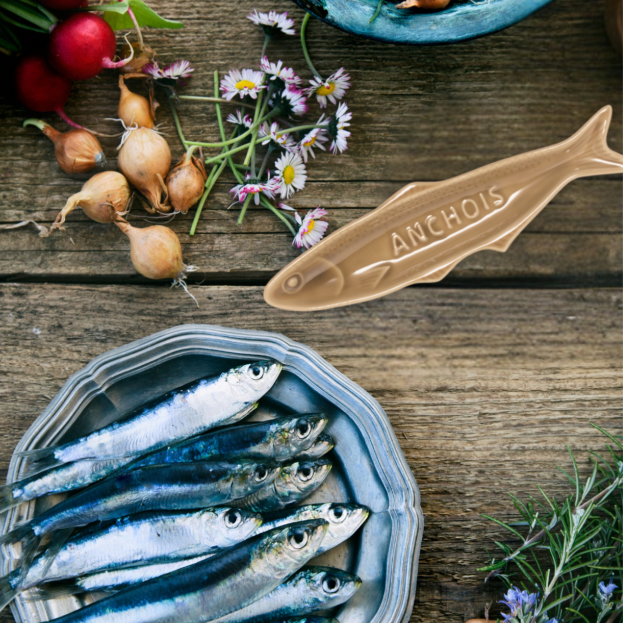 Container of anchovies on a wooden surface with a fish-shaped container labeled 'Anchois'.
