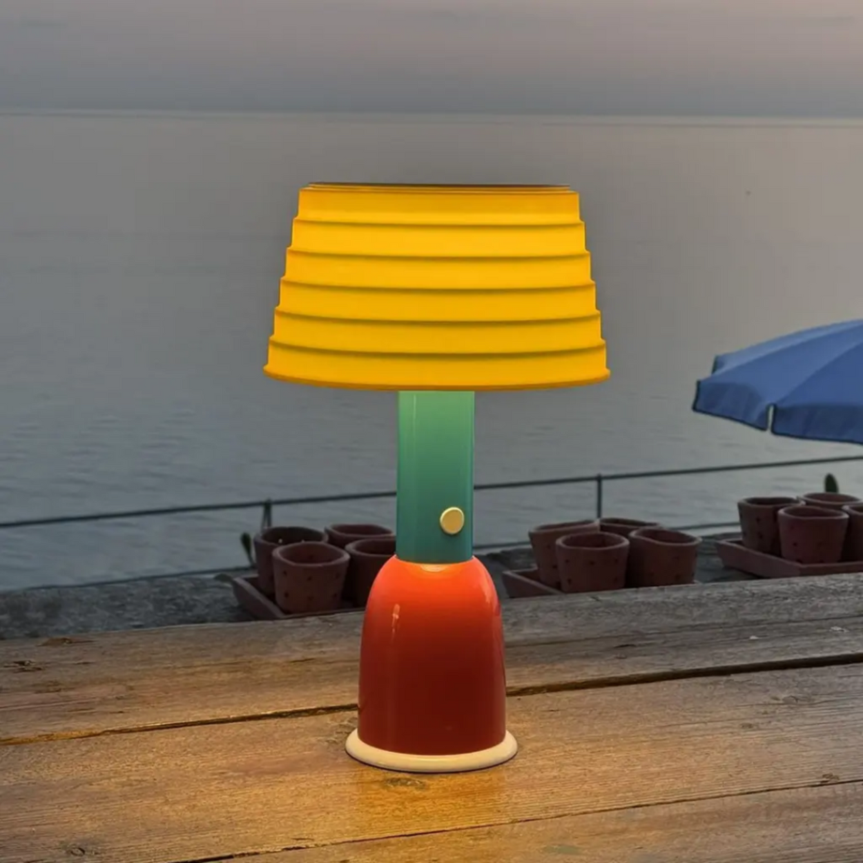 Colorful lamp with a yellow shade on a wooden surface by a body of water.