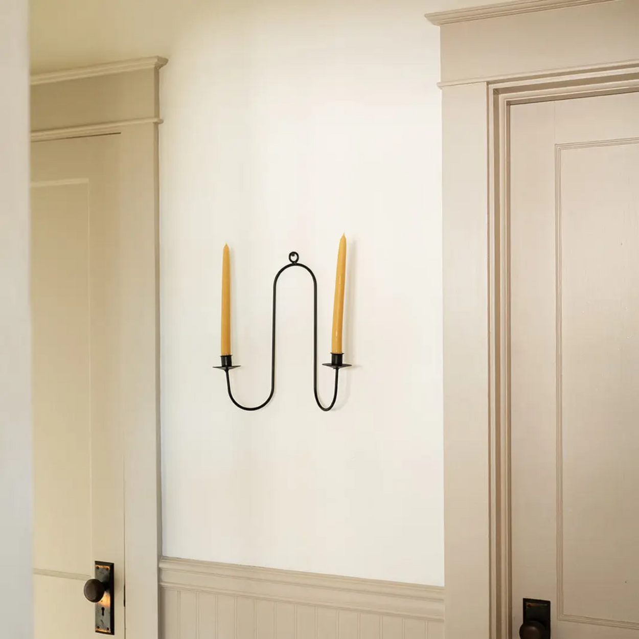 Wall-mounted candle holder with two candles on a white wall.