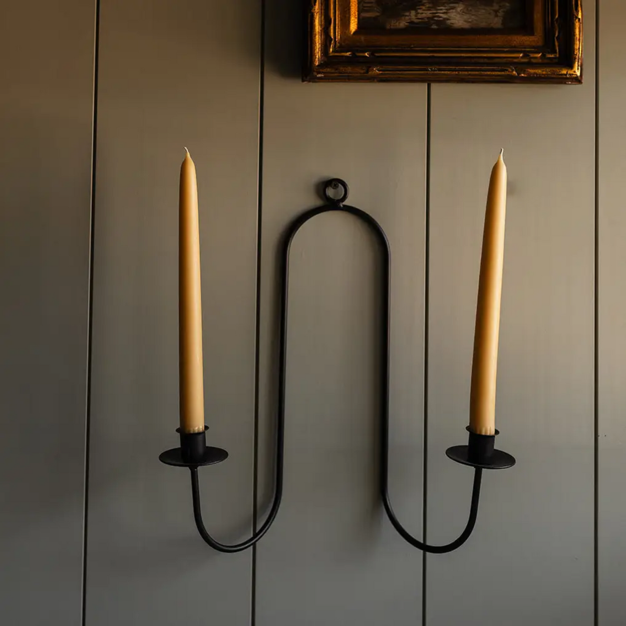 Two wall-mounted candle holders with candles on a gray wall.