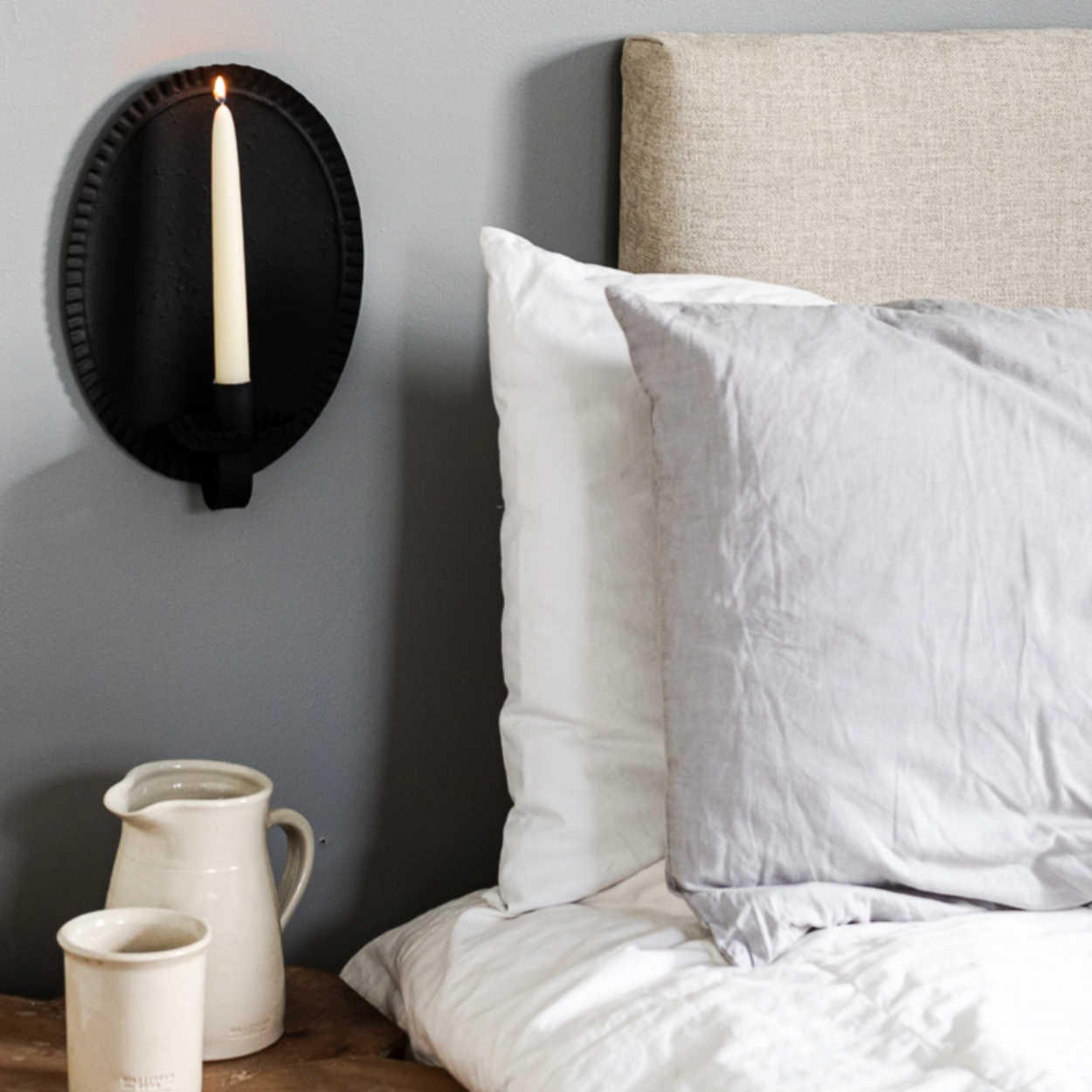 Bedroom setting with a wall sconce, pitcher, and cups on a nightstand.