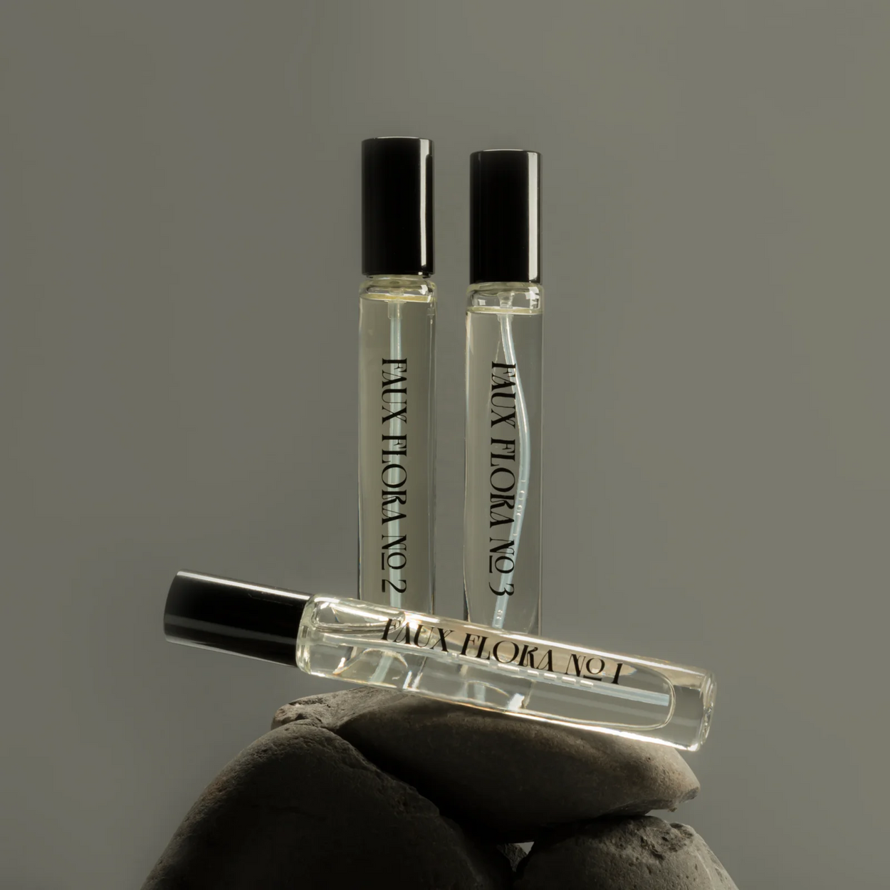 Three small perfume bottles balanced on grey stone against a grey background