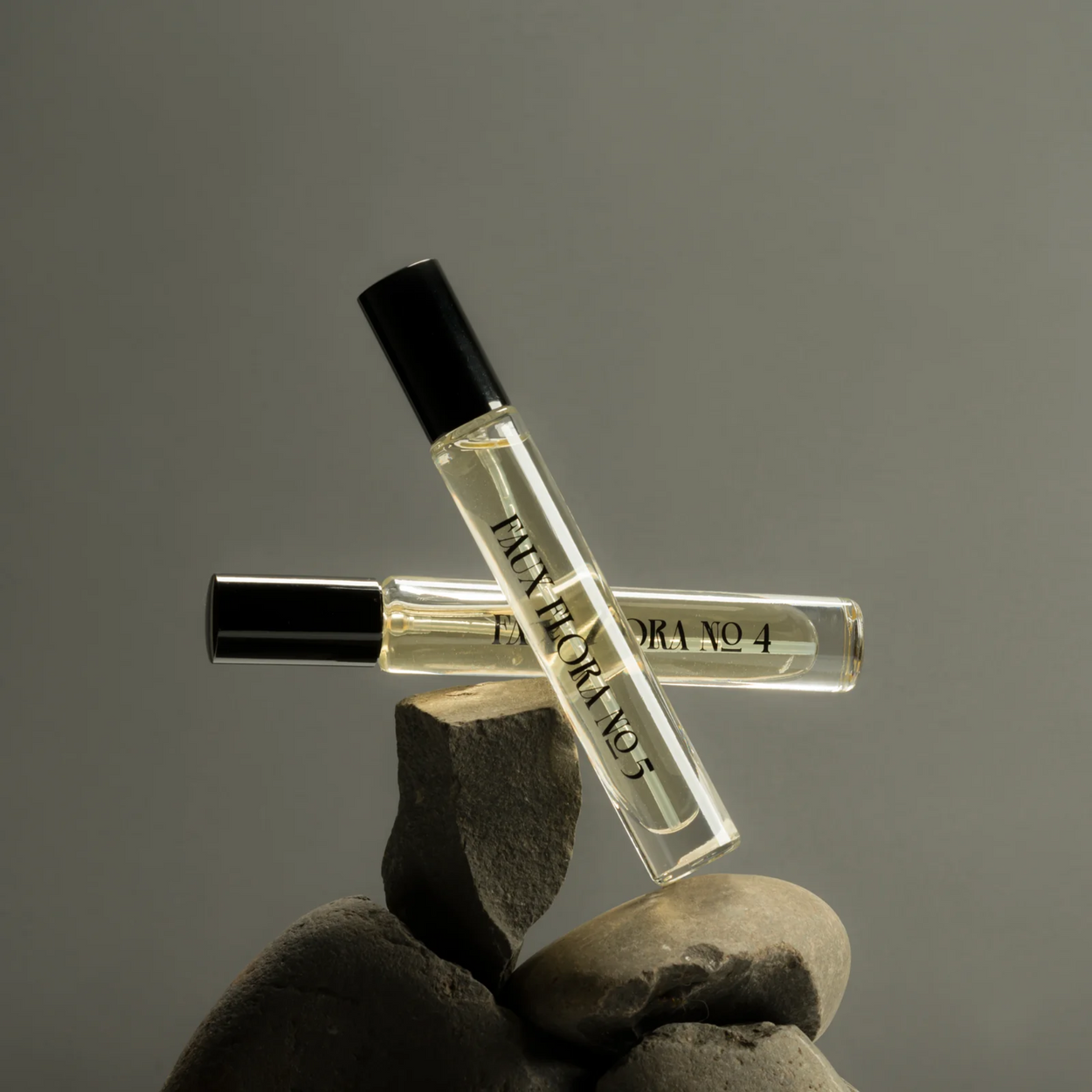 Two small perfume bottles with black caps on rocks against a grey background