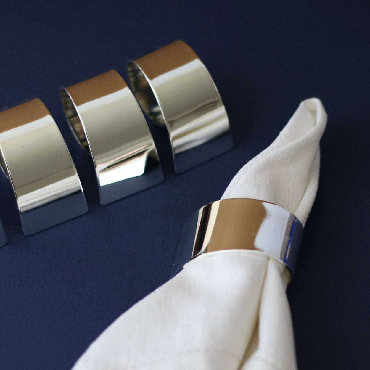 Close up, Vintage 2 sets of 4 silver plate napkin rings against dark blue backdrop.