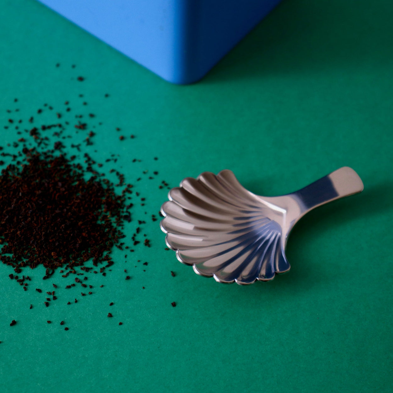 Japanese Shell Tea Spoon with tea leaves on a green background.