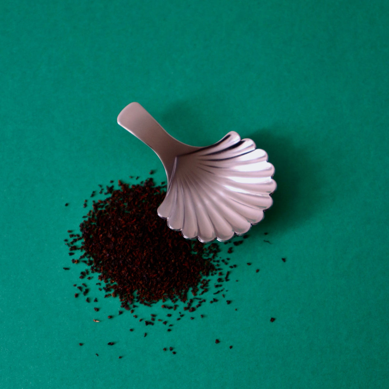 Japanese Shell Tea Spoon with tea leaves on a green background.