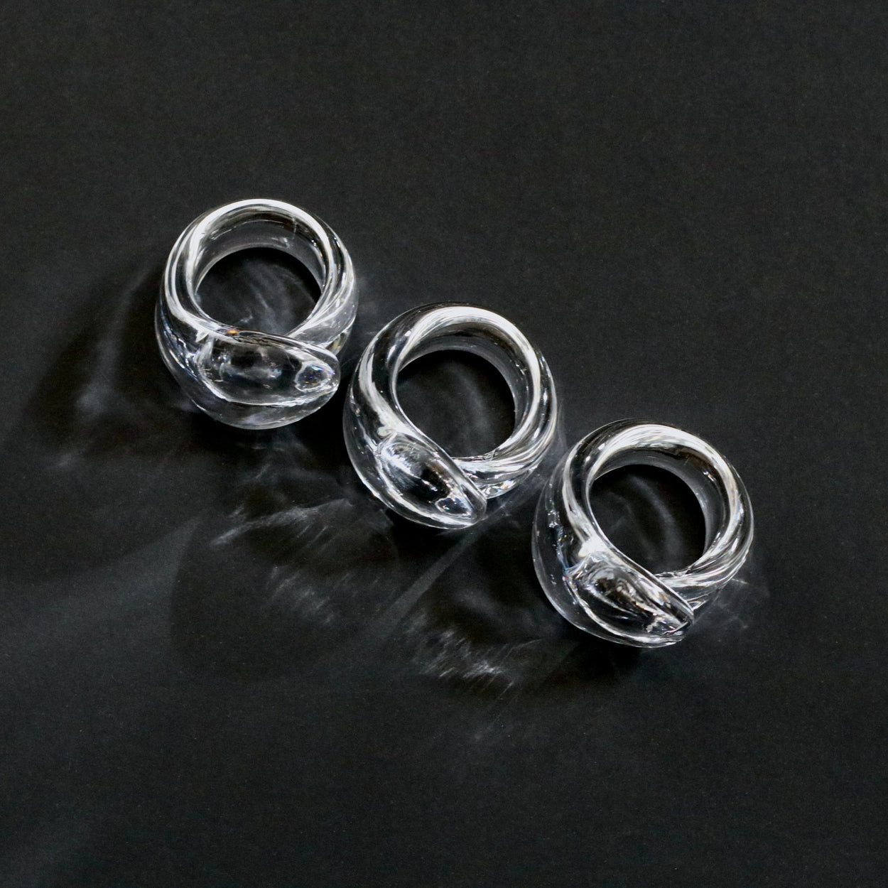 Vintage handmade glass napkin rings against a black background.