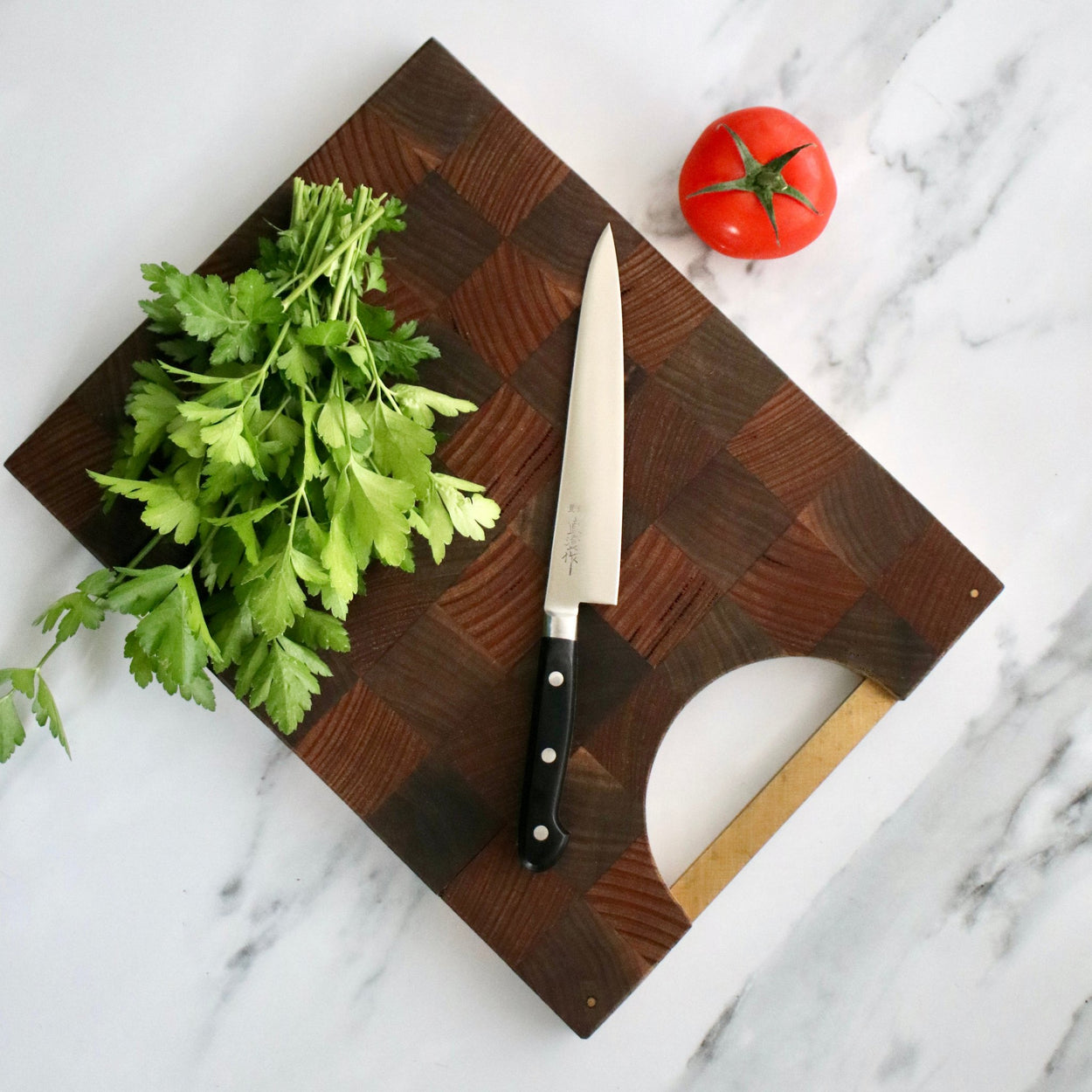 Japanese Naozumi Nihonkou 15cm Sharp Carbon Steel Kitchen Knife with tomato and parsley on wood cutting board, on marble bench.
