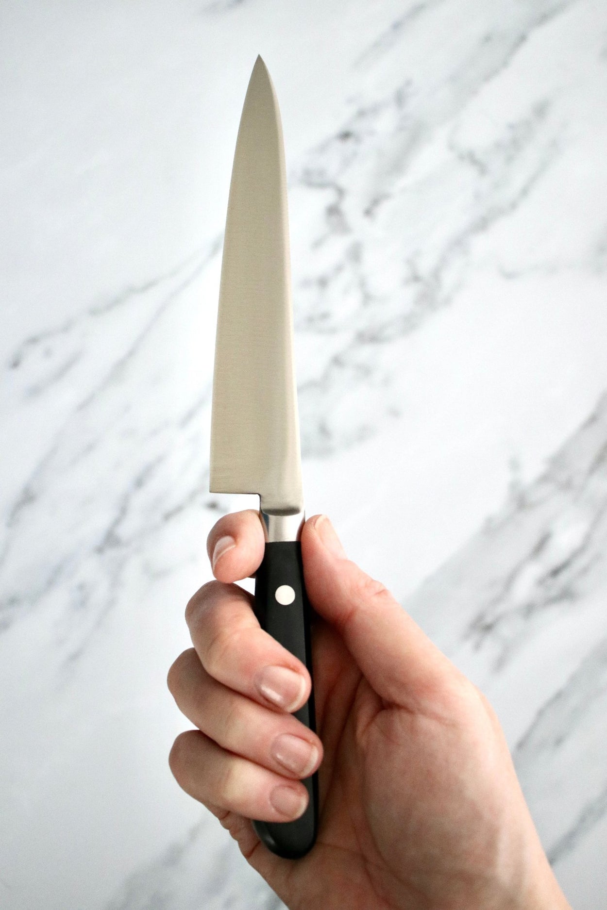 Hand holding Japanese Naozumi Nihonkou 15cm Sharp Carbon Steel Kitchen Knife and packaging on marble bench.