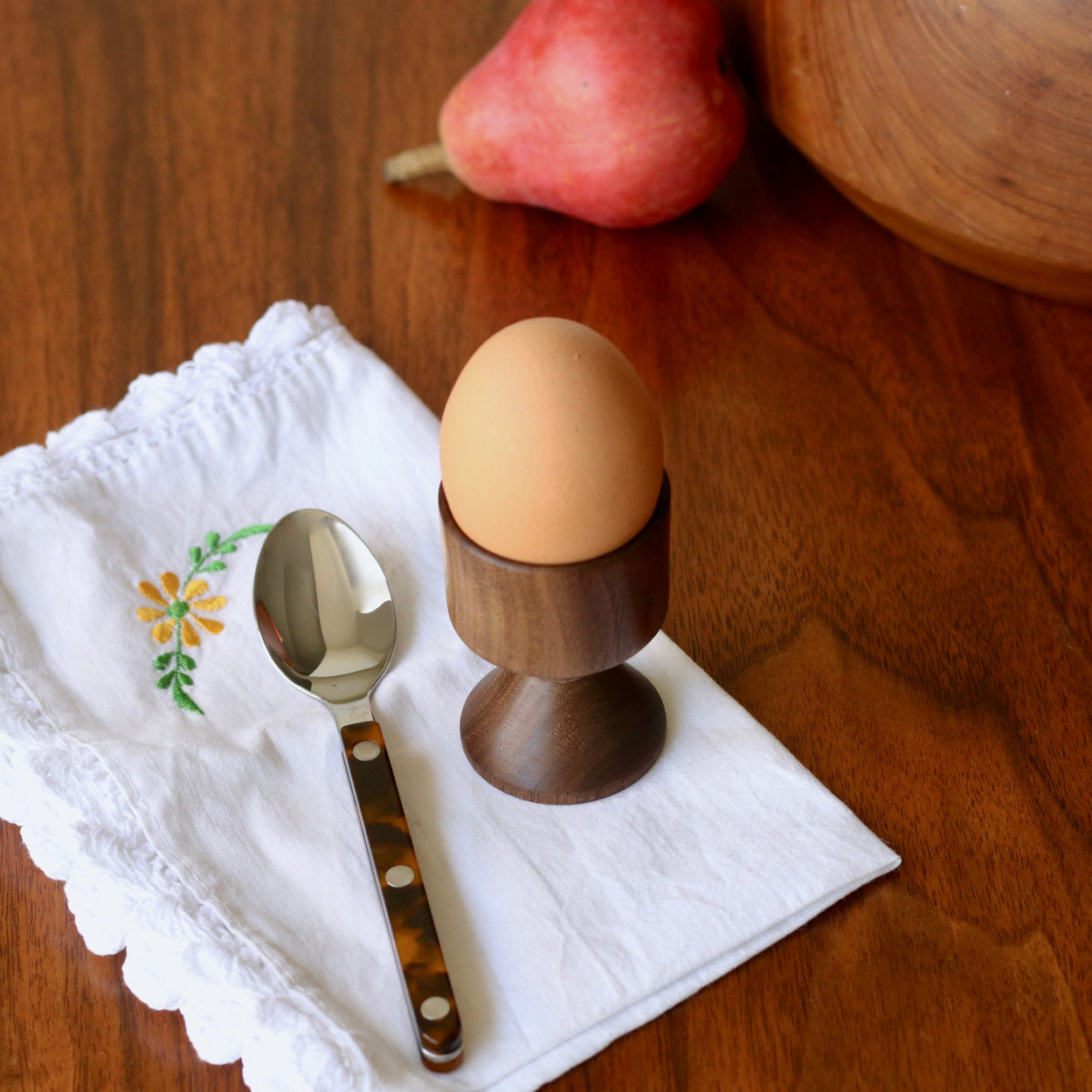 Hand crafted walnut wood egg cup with egg and Sabre Paris spoon and napkin on wood tabletop