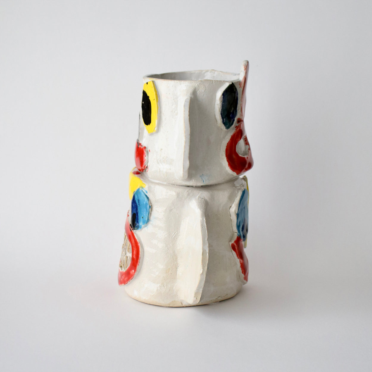 Ceramic vase with colourful face designs on a light gray background