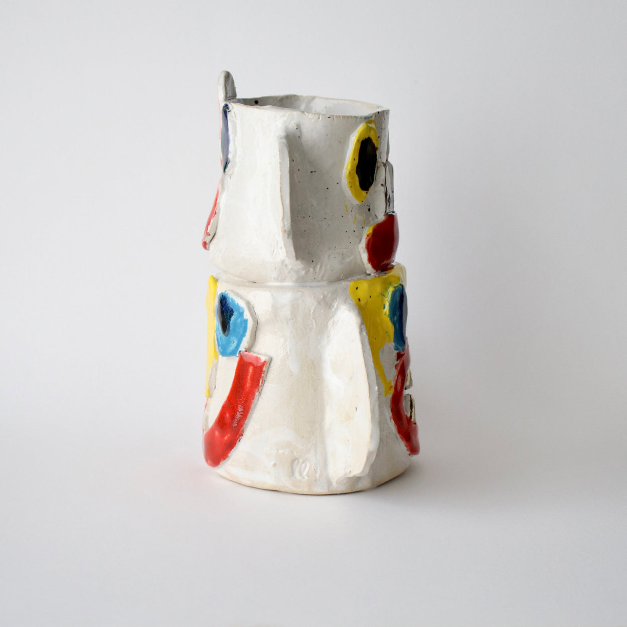Ceramic vase with colourful face designs on a light grey background