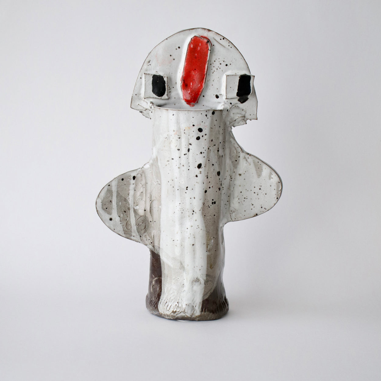 Ceramic sculpture with a white body, black speckles, and a red nose on a light grey background