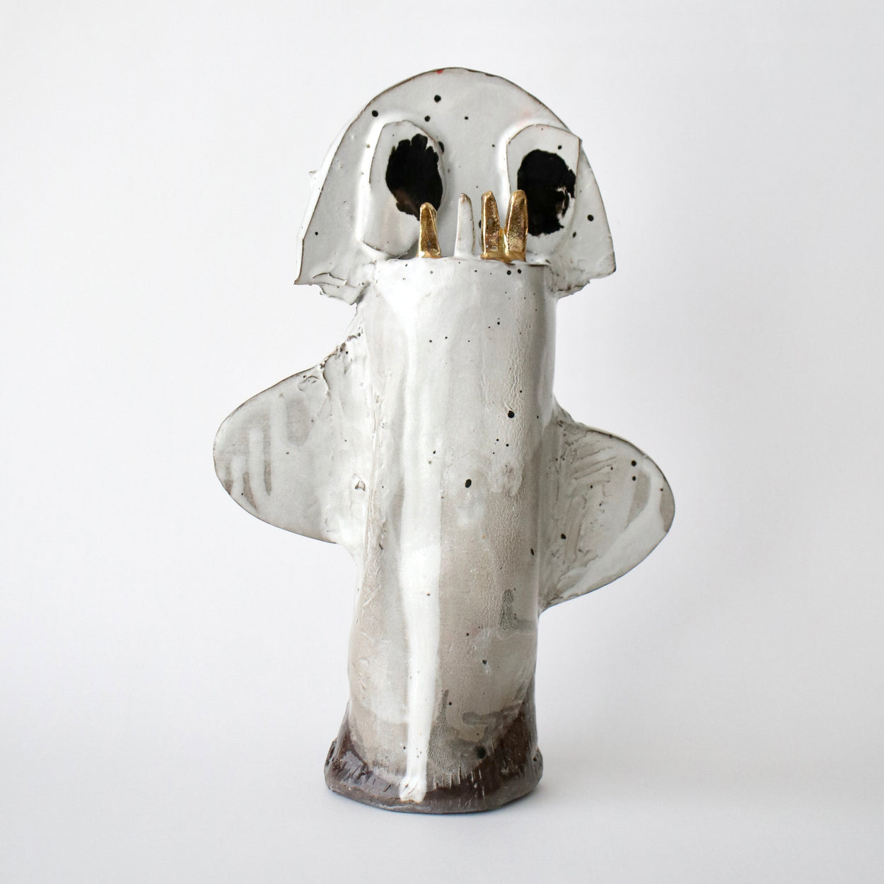 Ceramic sculpture of a ghost with black eyes and gold accents on a white background