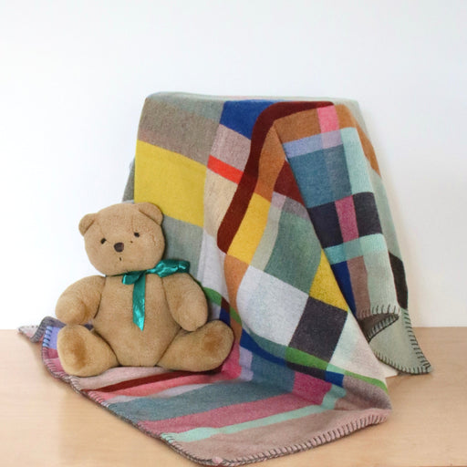 Multicolored patchwork blanket draped over a surface with a teddy bear sitting on it.