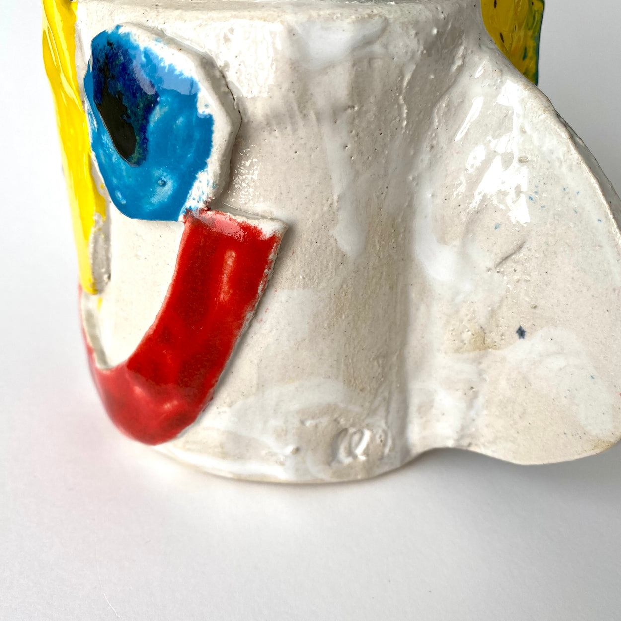 Close up of ceramic face vase with red, blue, and yellow colours on a white background