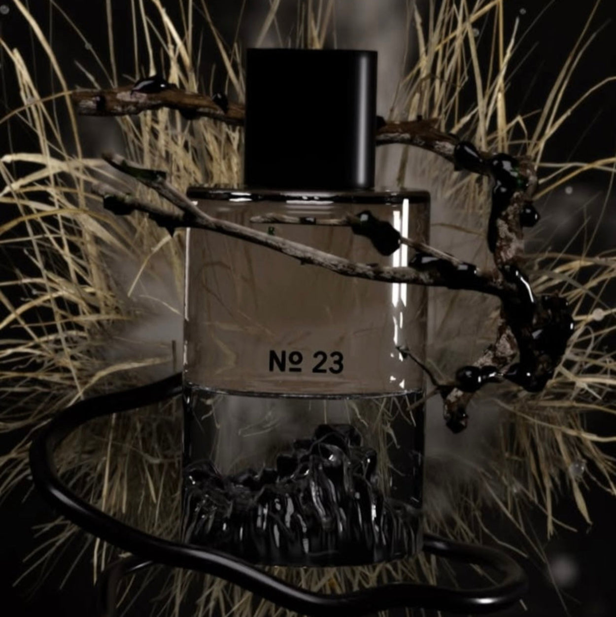 Perfume bottle labeled 'No. 23' surrounded by grass and branches on a dark background