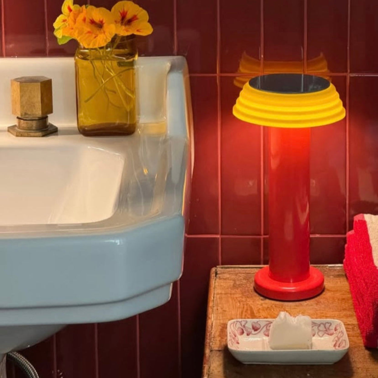 Bathroom setting with a sink, lamp, and decorative elements on a red tiled wall.