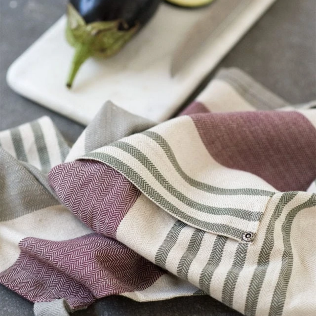 Close up of a Mungo cotton linen chefs apron, eggplant and chopping board and knife.