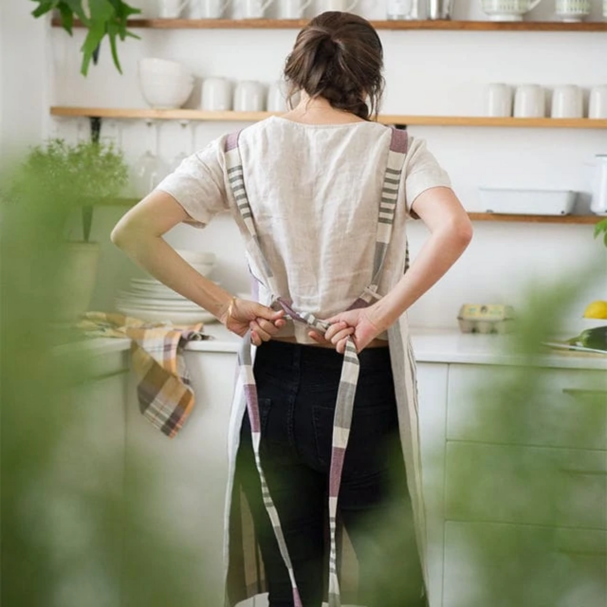 Woman with a pony tail and her back to us tying up a Mungo cotton linen chefs apron.