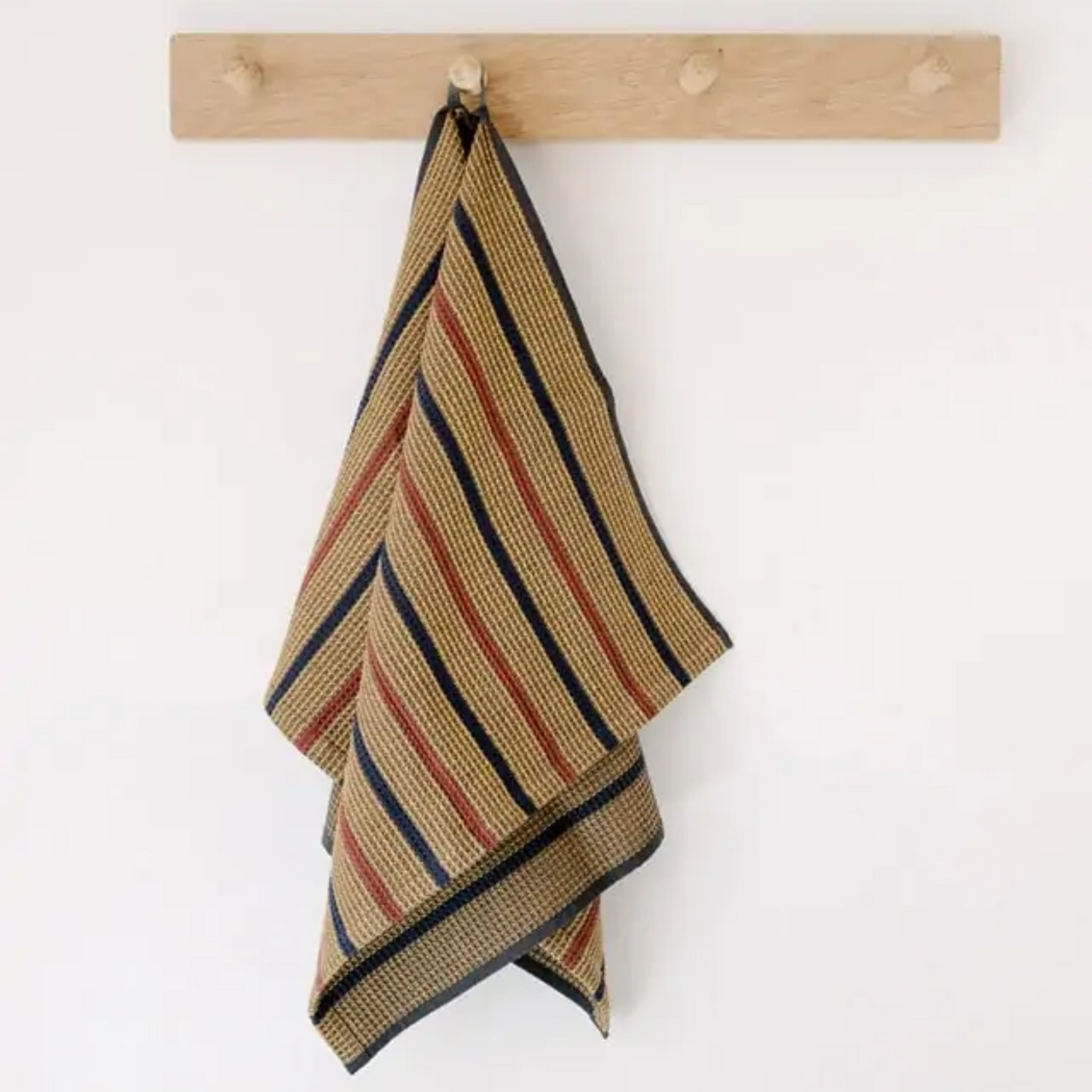 Mungo Waffle Tea Towel in Ochre brown hanging on wood hooks.