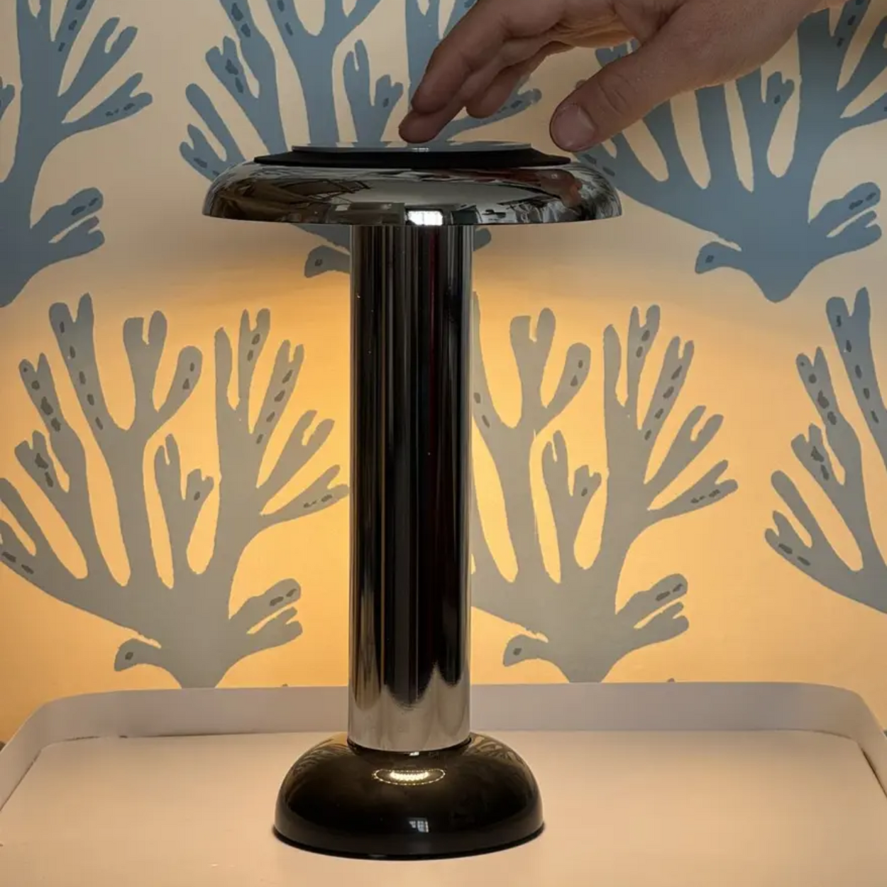 Chrome Sowden PL6 lamp with a hand interacting with it against a patterned background