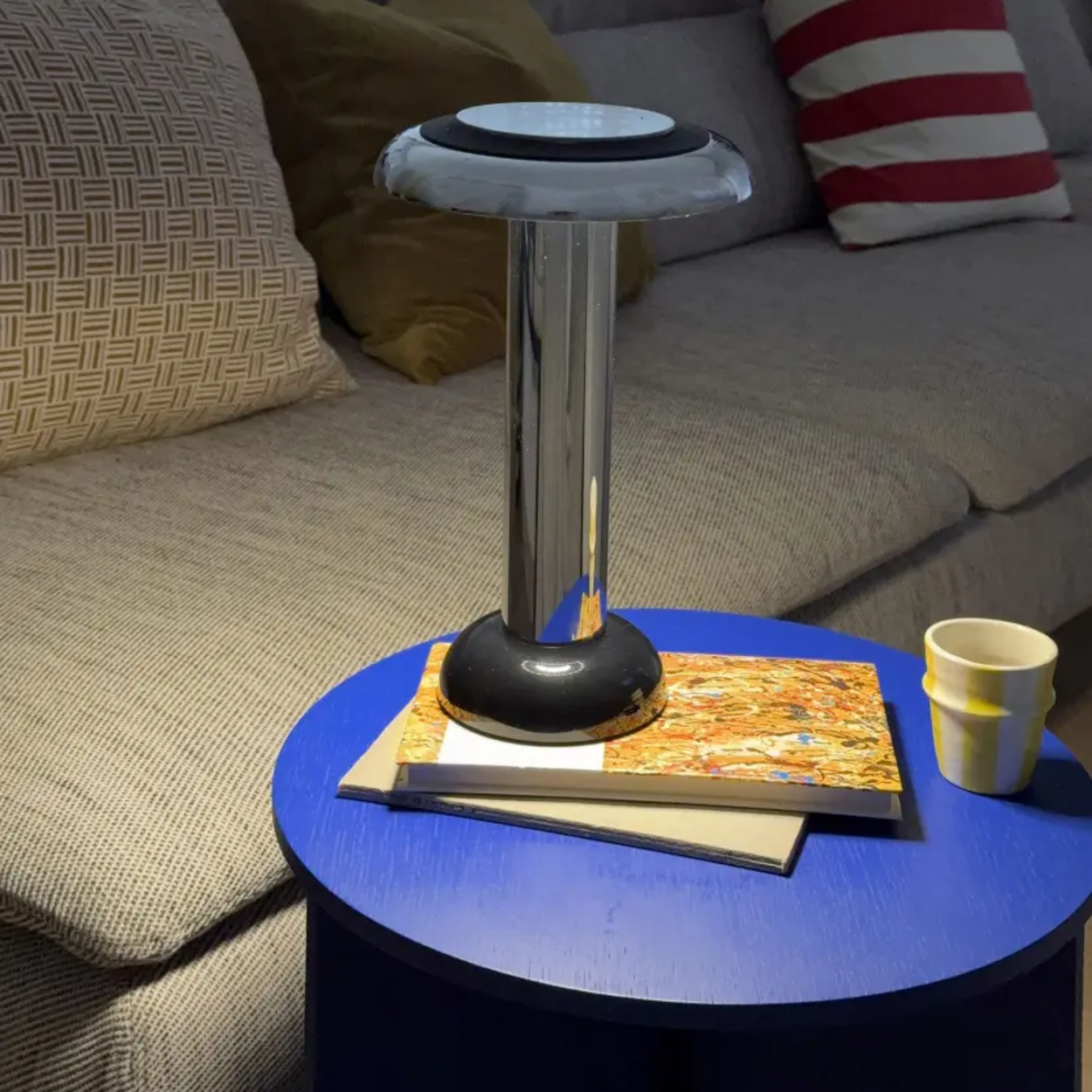 Blue round table with a black and silver Sowden PL6 lamp in front of a gray sofa with pillows.