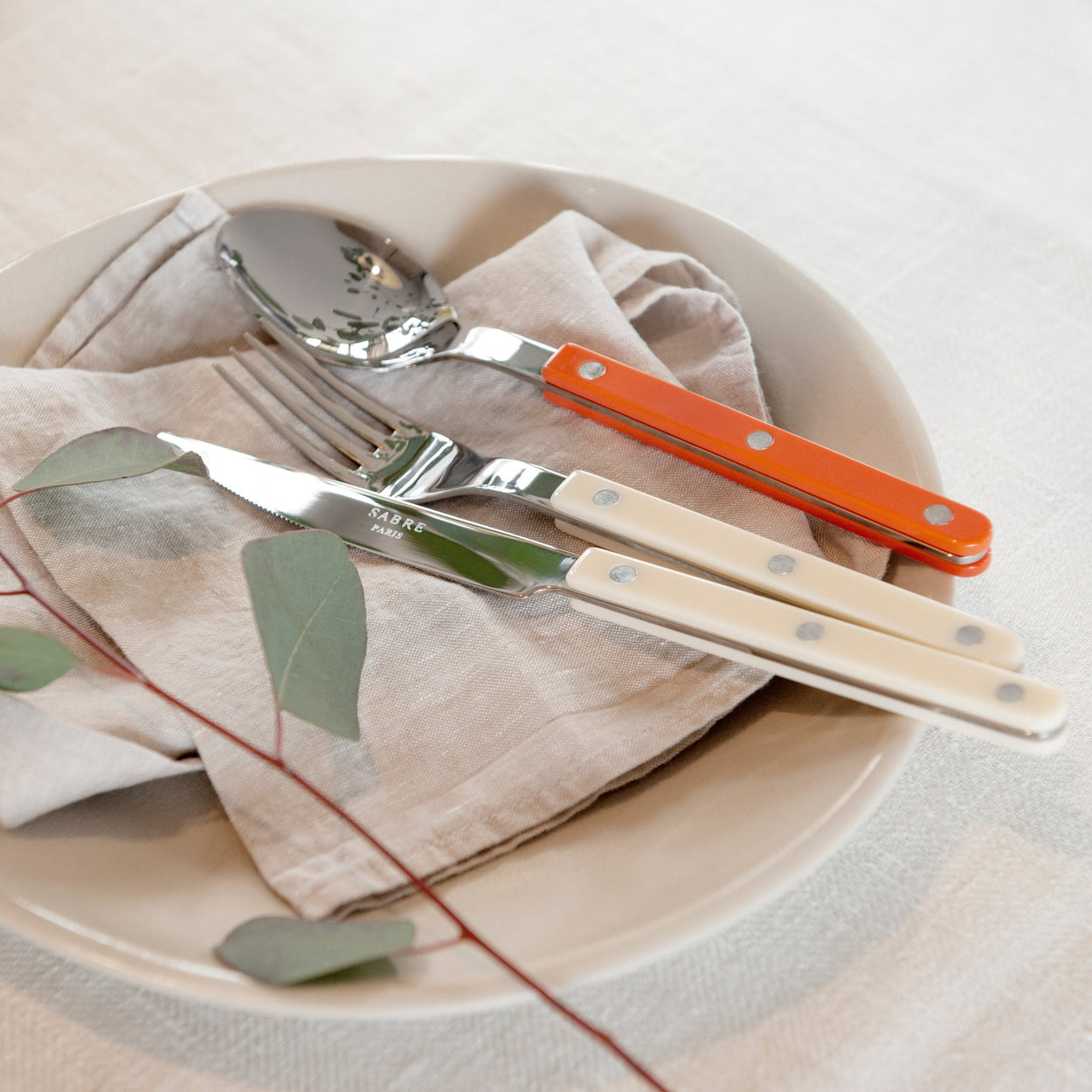 Sabre Bistrot Cutlery 4 Piece Set - Ivory and orange on beige plate