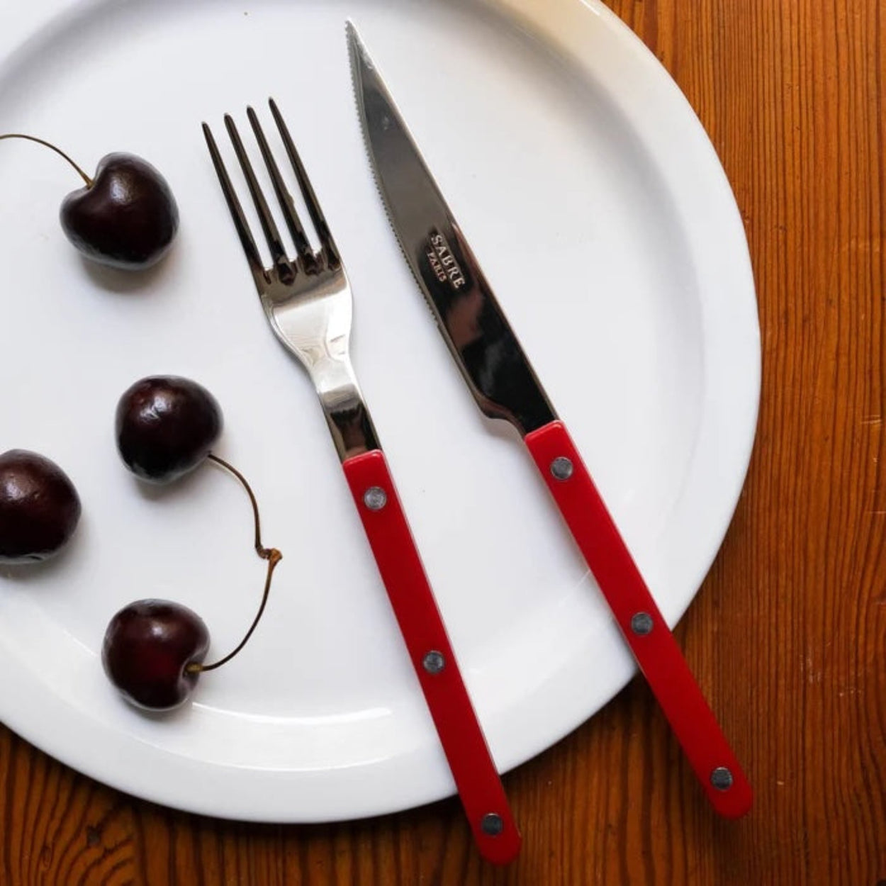 Sabre Paris Burgundy 4 piece flatware set, on wood tabletop.