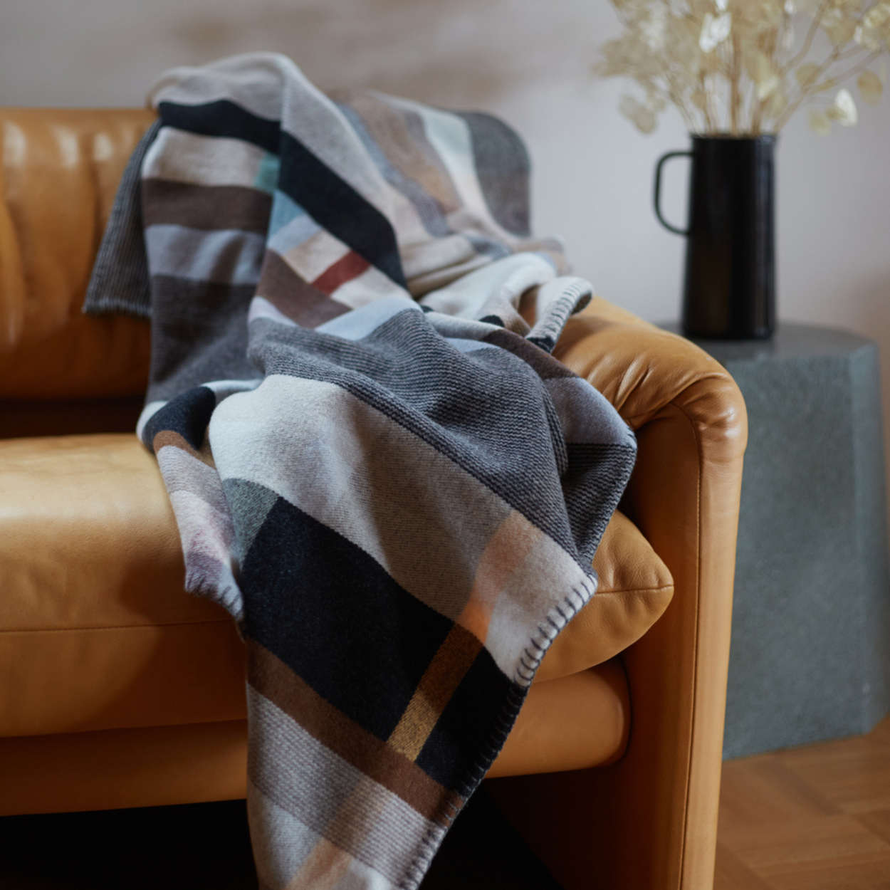 Wallace Sewell Premium Chippendale Merino lambswool throw in pale brown tones, draped on caramel leather armchair.