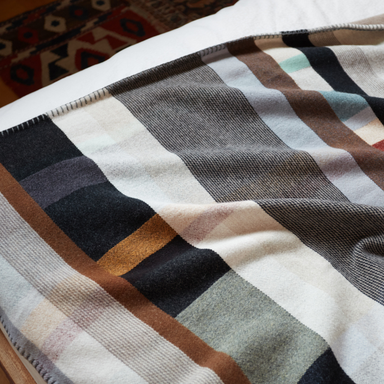 Wallace Sewell Premium Chippendale Merino lambswool throw in pale brown tones, closeup on bed.
