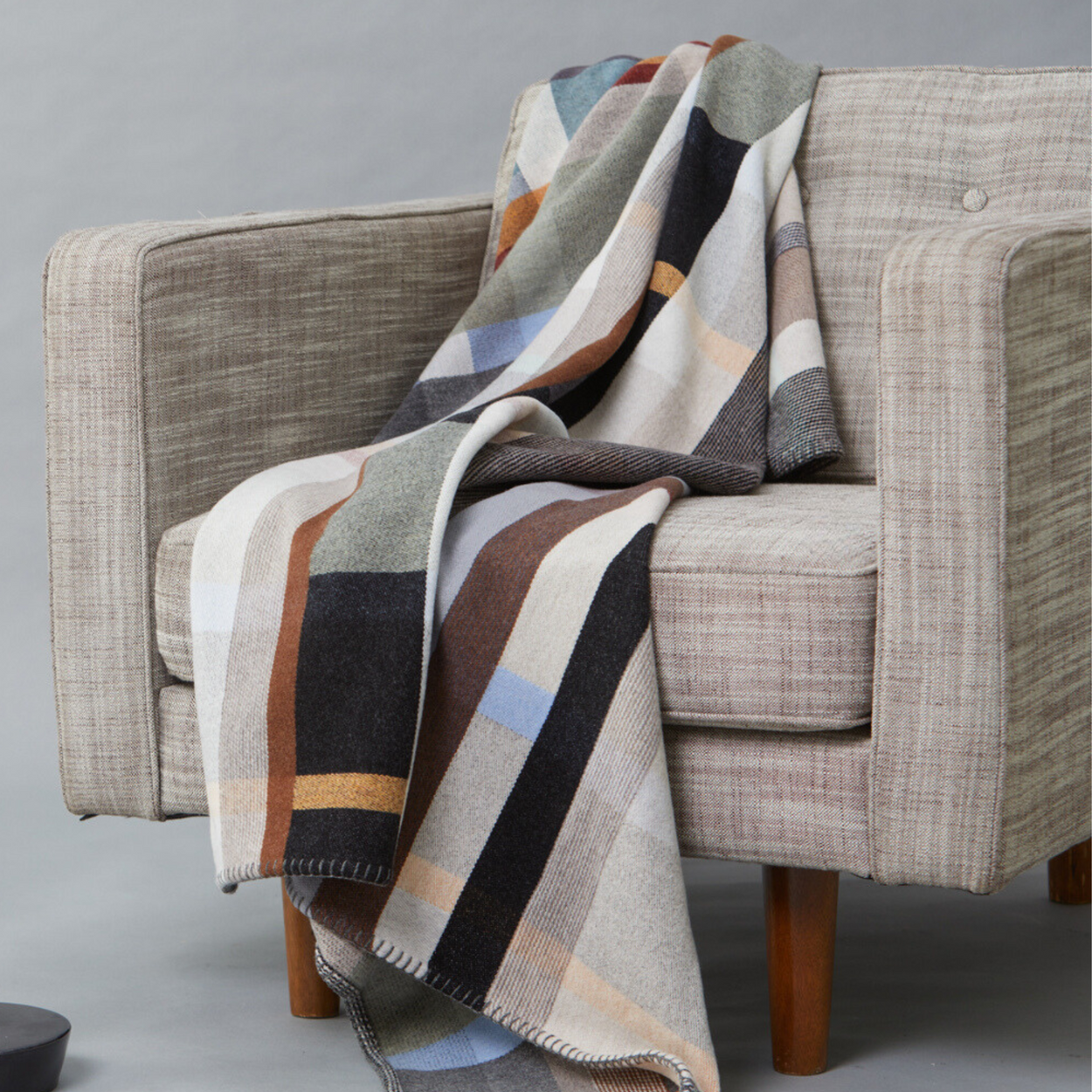Wallace Sewell Premium Chippendale Merino lambswool throw in pale brown tones, draped on arm chair.