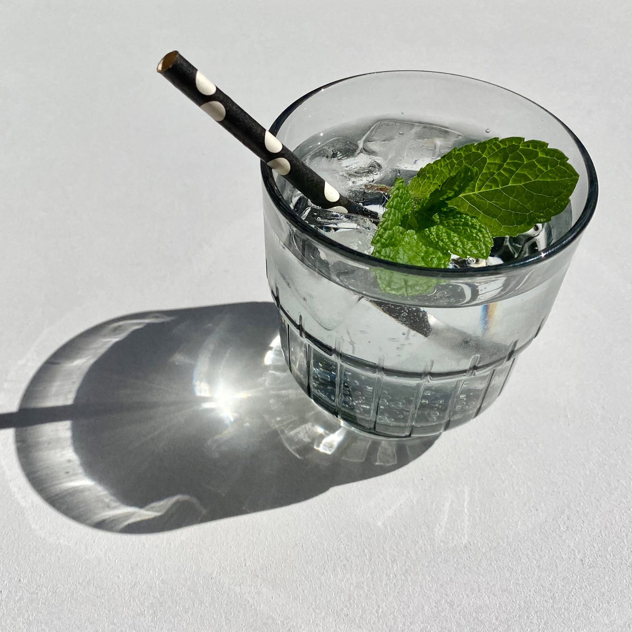 Smoky Grey Portuguese glass with polka dot straw and mint leaf in water with white background.