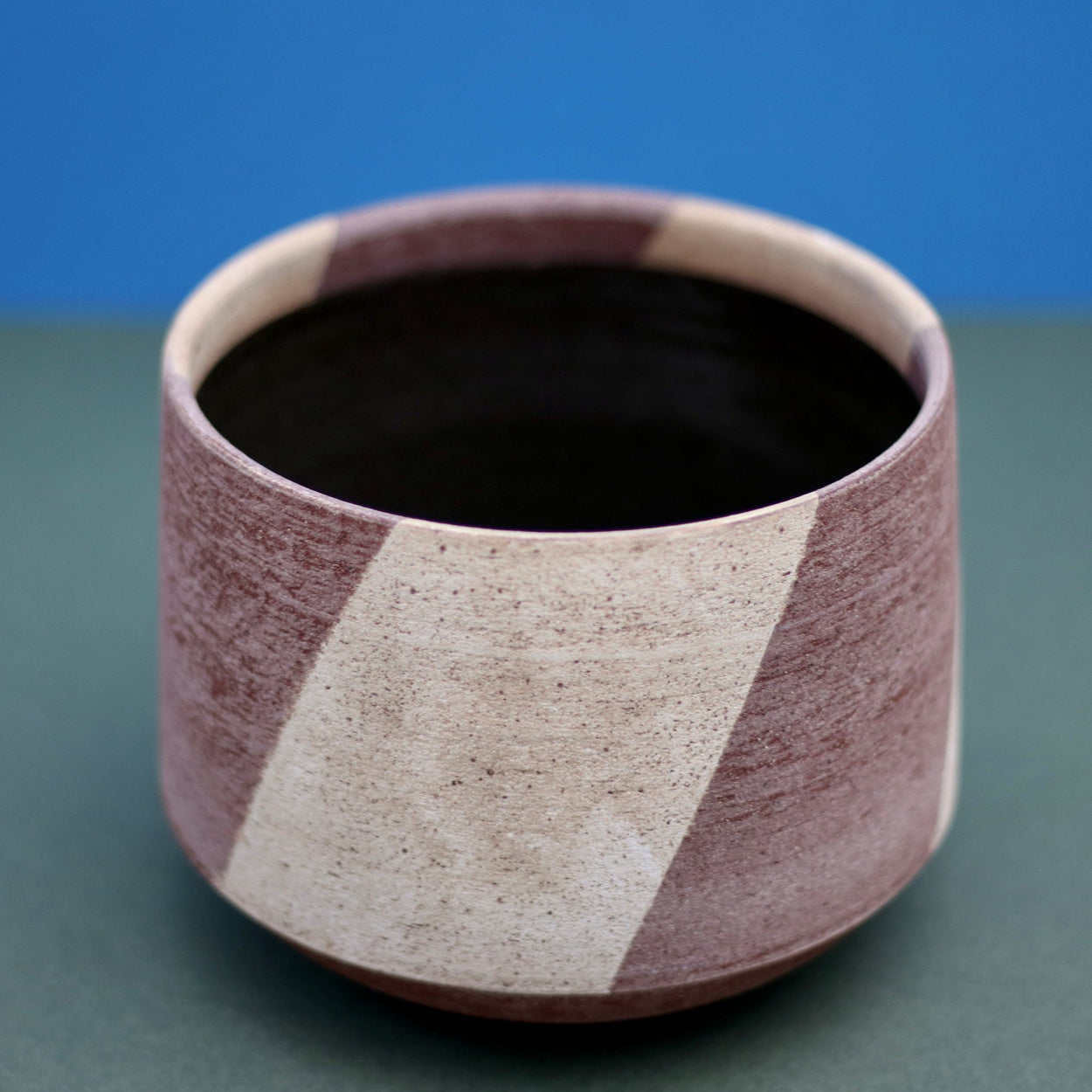 Ceramic Stripe Bowl by Amanda-Sue Rope with blue green background. Top angle view.