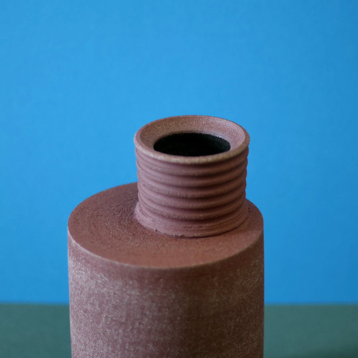 Close up of Handmade Ceramic Vase by Amanda-Sue Rope against a blue and green background.