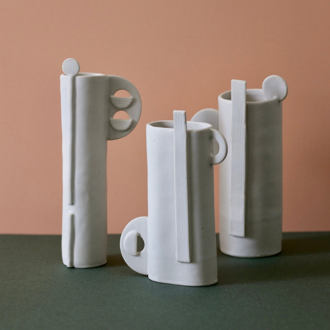 Three white Cassie Hansen Vases against green and peach background, front view.