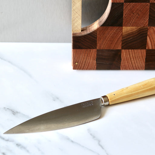 Pallares Solsona 16cm Box Wood Carbon Steel Kitchen Knife on white marble bench with wood cutting board behind.