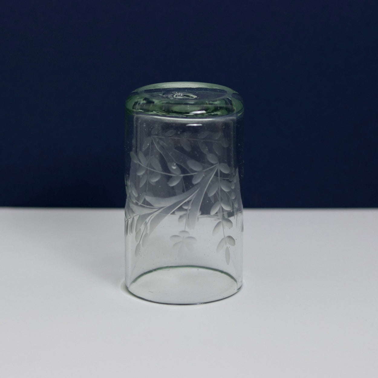 Upside down Hand blown etched glass tumbler with blue and white background.