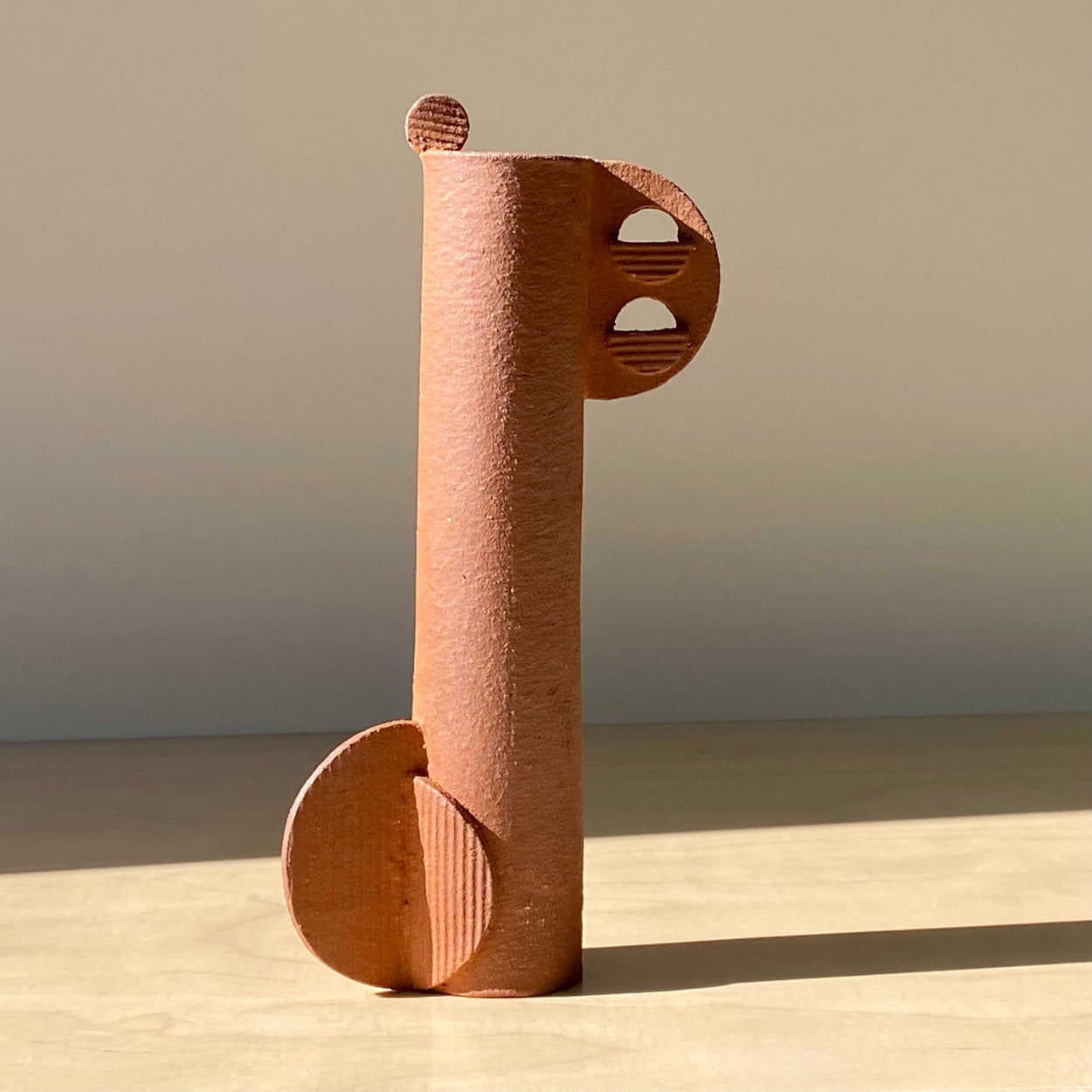 Cassie Hansen Tall Sculpture on pale wood table with hard shadow.