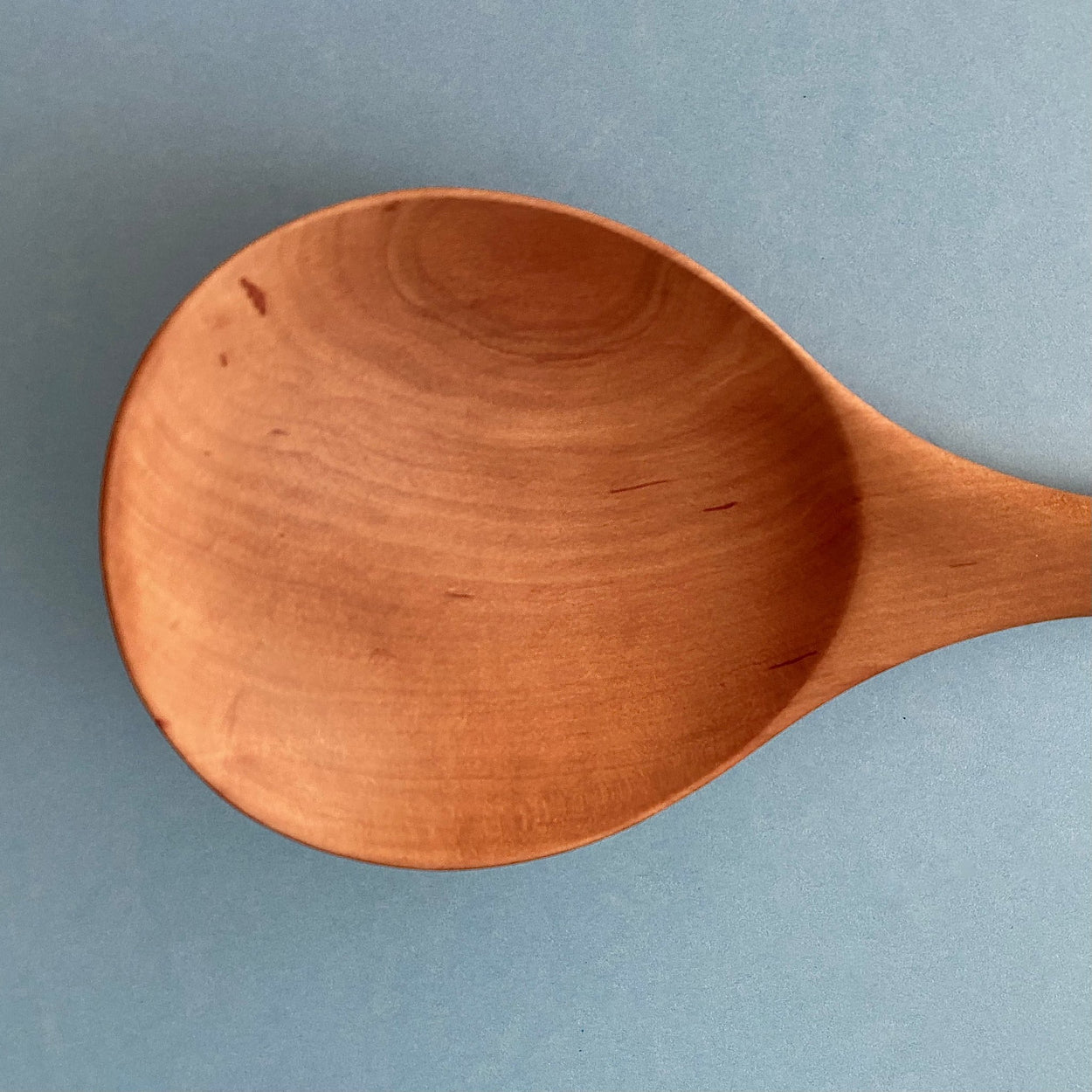 Handmade Pear Wood Soup Ladle, close up, against blue background.