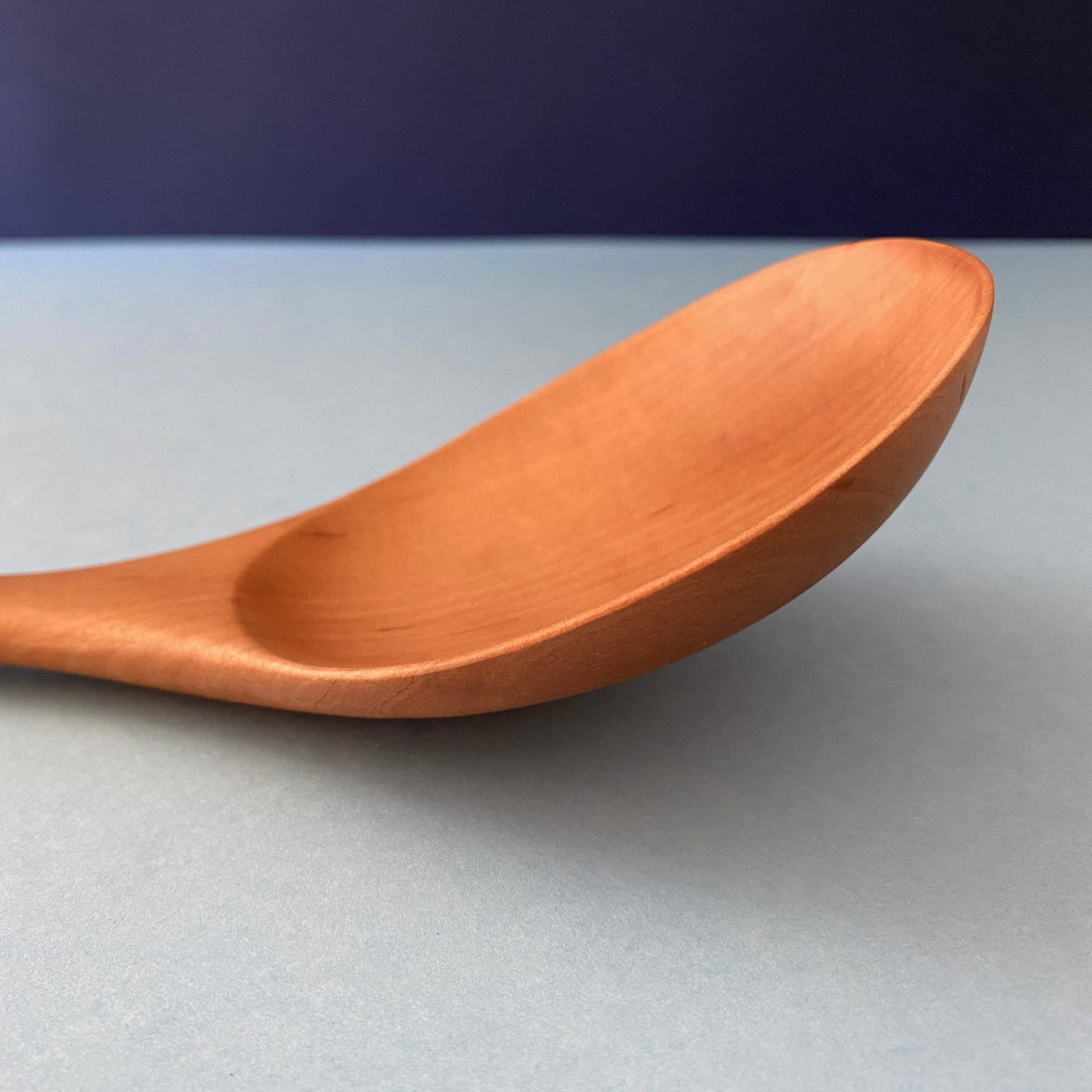 Handmade Pear Wood Soup Ladle lying against blue backdrop, close up.
