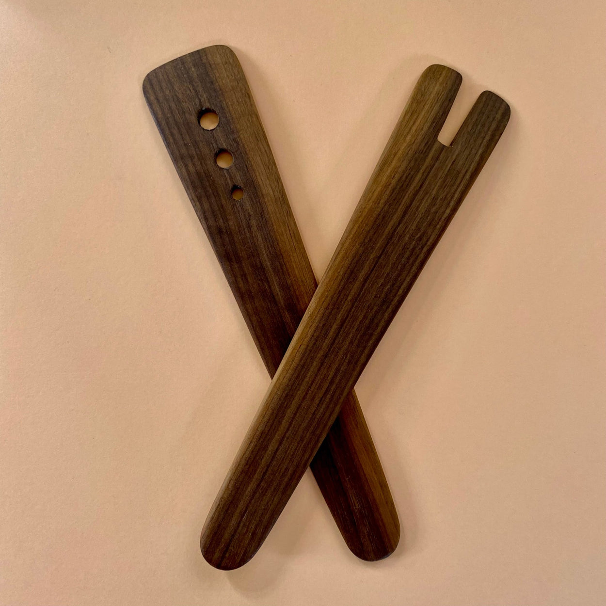 Handmade Walnut Wood Salad Servers upright and crossed against a peach and chocolate background. By Civil Dawn Studio.