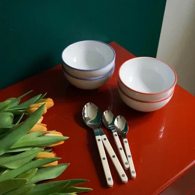 Ivory Sabre Paris Bistrot cutlery on a red tabletop with white bowls and orange tulips.