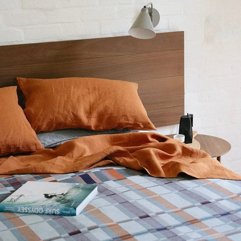 Mungo Double Cloth blanket in Seven Seas colour on bed with terracotta pillows and sheet.