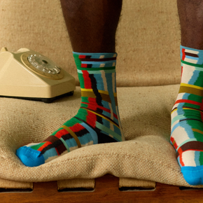Man standing on couch wearing Bonne Maison Blue Grid socks with cream retro telephone.