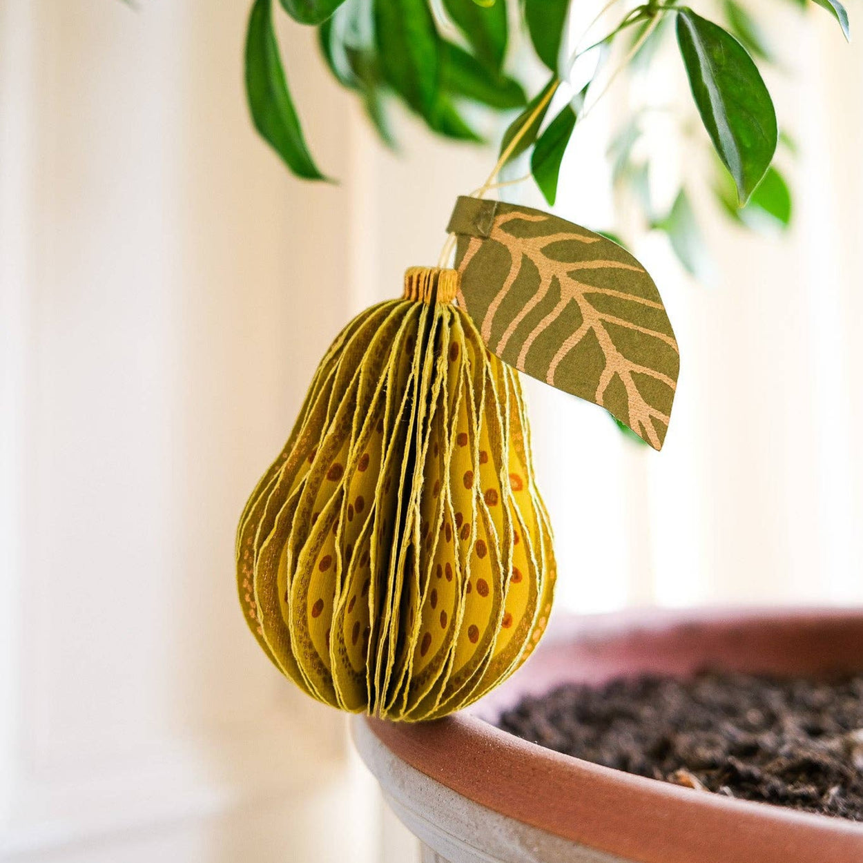 Decorative paper fruit hanging from a plant with a blurred background