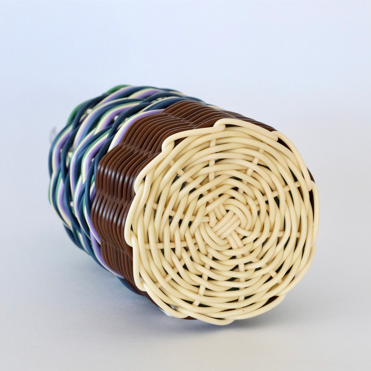 Base of Decorative olive oil bottle with green, brown and navy woven design and metallic nozzle on a white background.